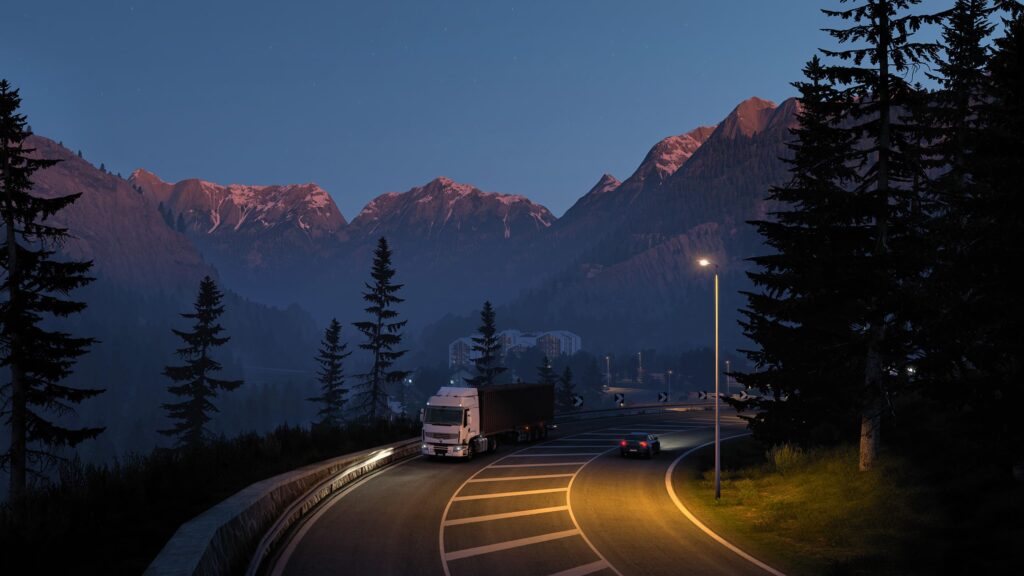 A screenshot from Euro Truck Simulator 2 showing a truck travelling through a scenic mountain pass at sunset. 